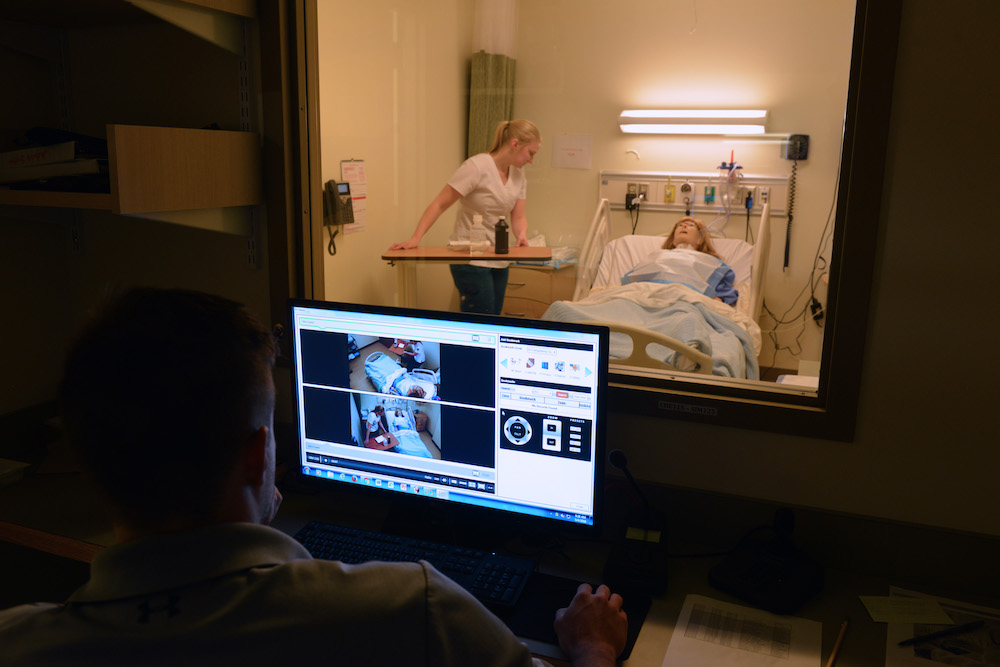 A computer monitors a female nursing 첥 working with an adult patient simulation